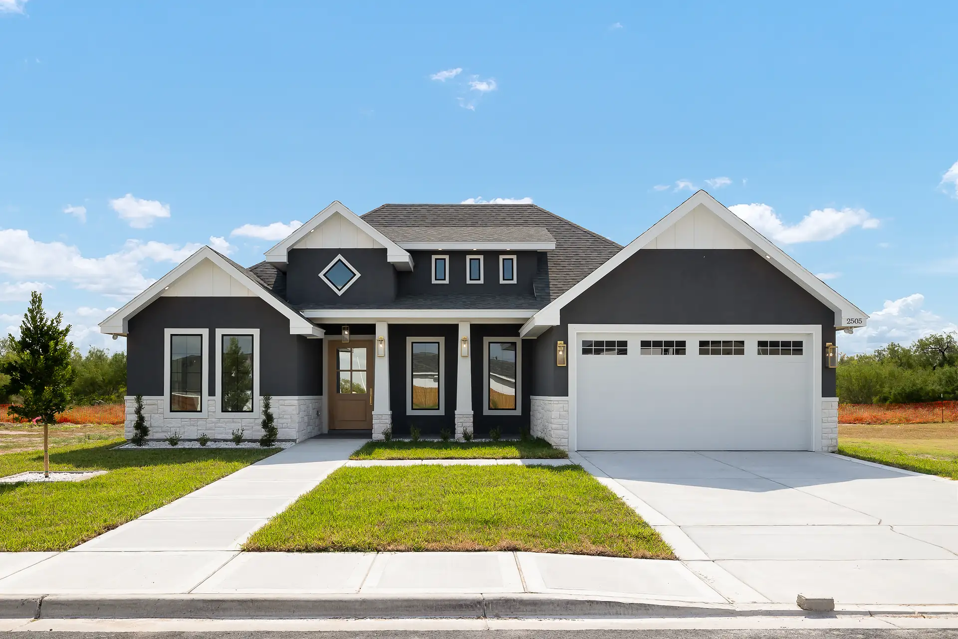 Front exterior of the 2505 Northgate custom home — gray stucco with white trim, two-car garage, diamond accent window, columned entry porch